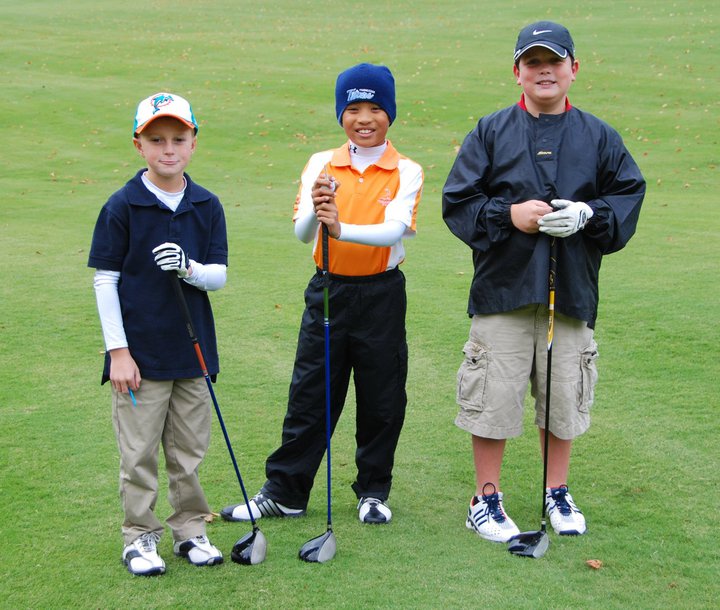 Three young boys are standing on a golf course.