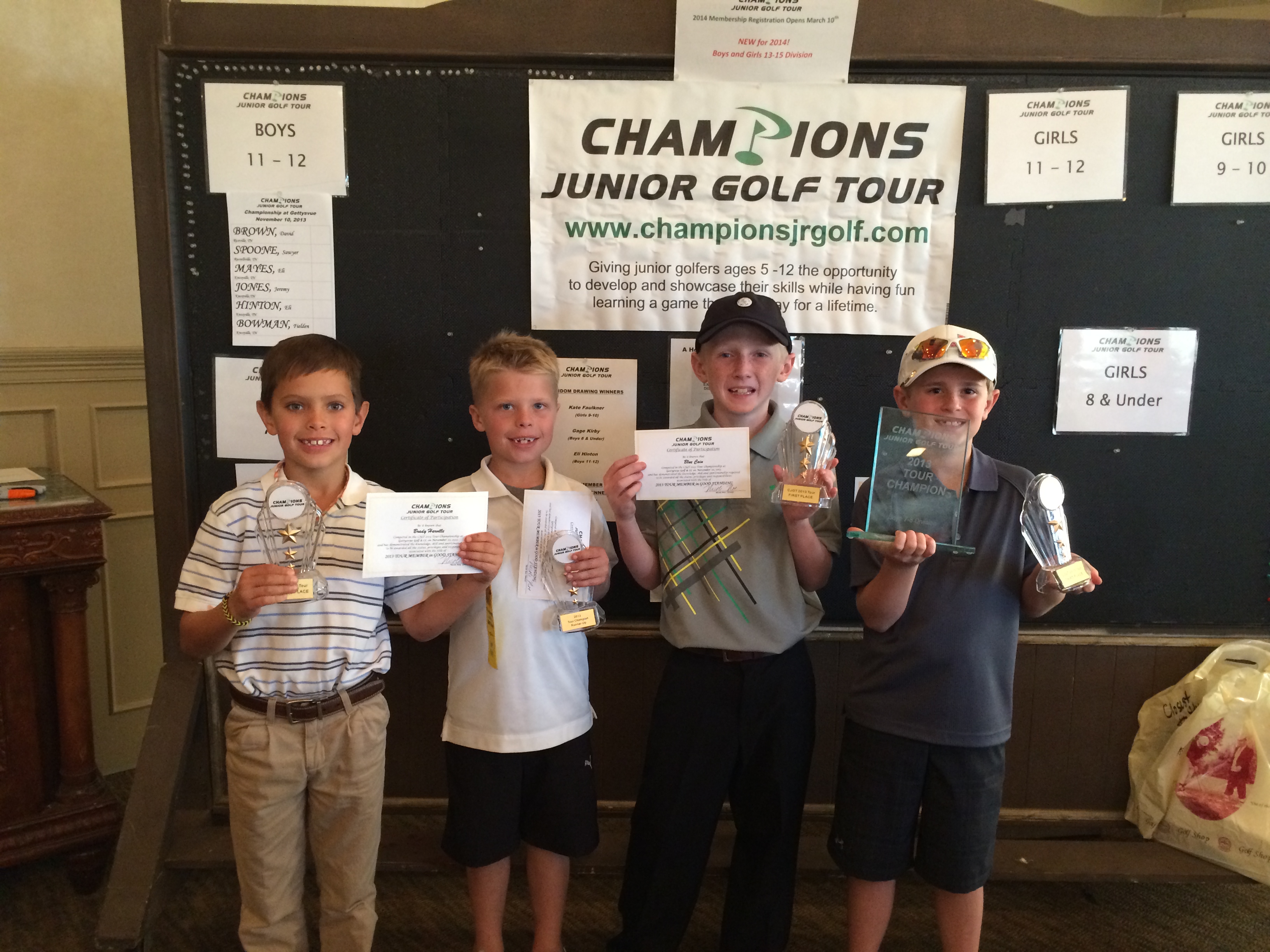 Four young boys holding up their prizes for winning a golf tournament.