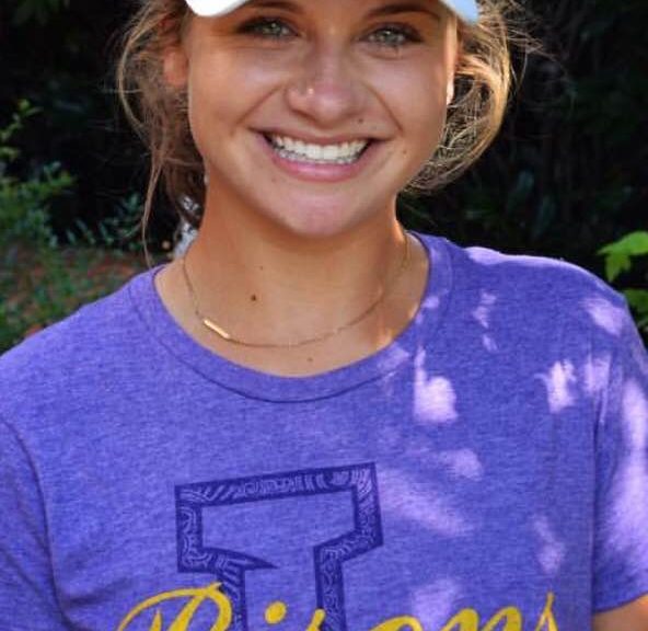 A woman in purple shirt wearing a white hat.